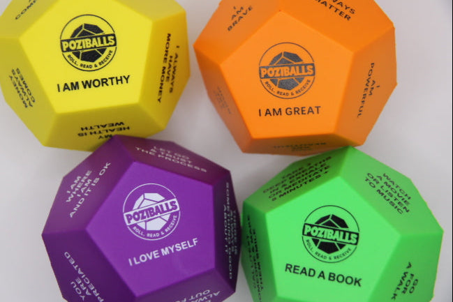 Four Dodecahedron-shaped stress ball in four colors orange, green, yellow and purple with 'Poziballs' branding and text in black and white letters on twelve sides